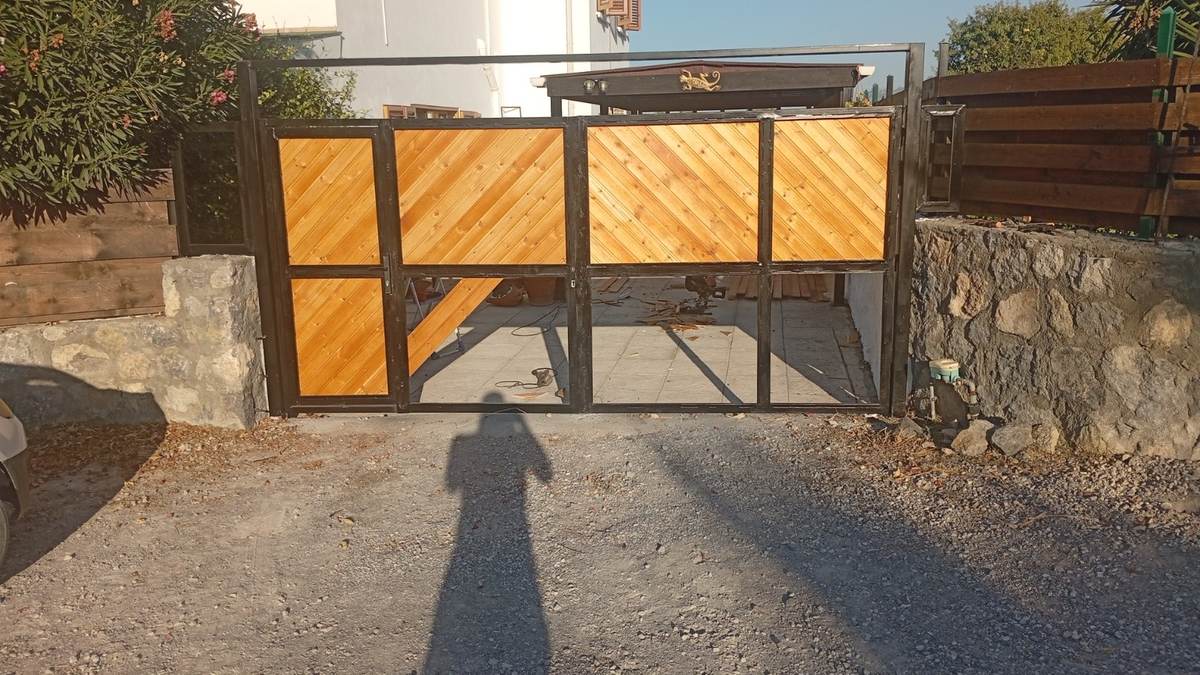 Custom driveway gate during construction with diagonal tongue-and-groove timber panels being fitted